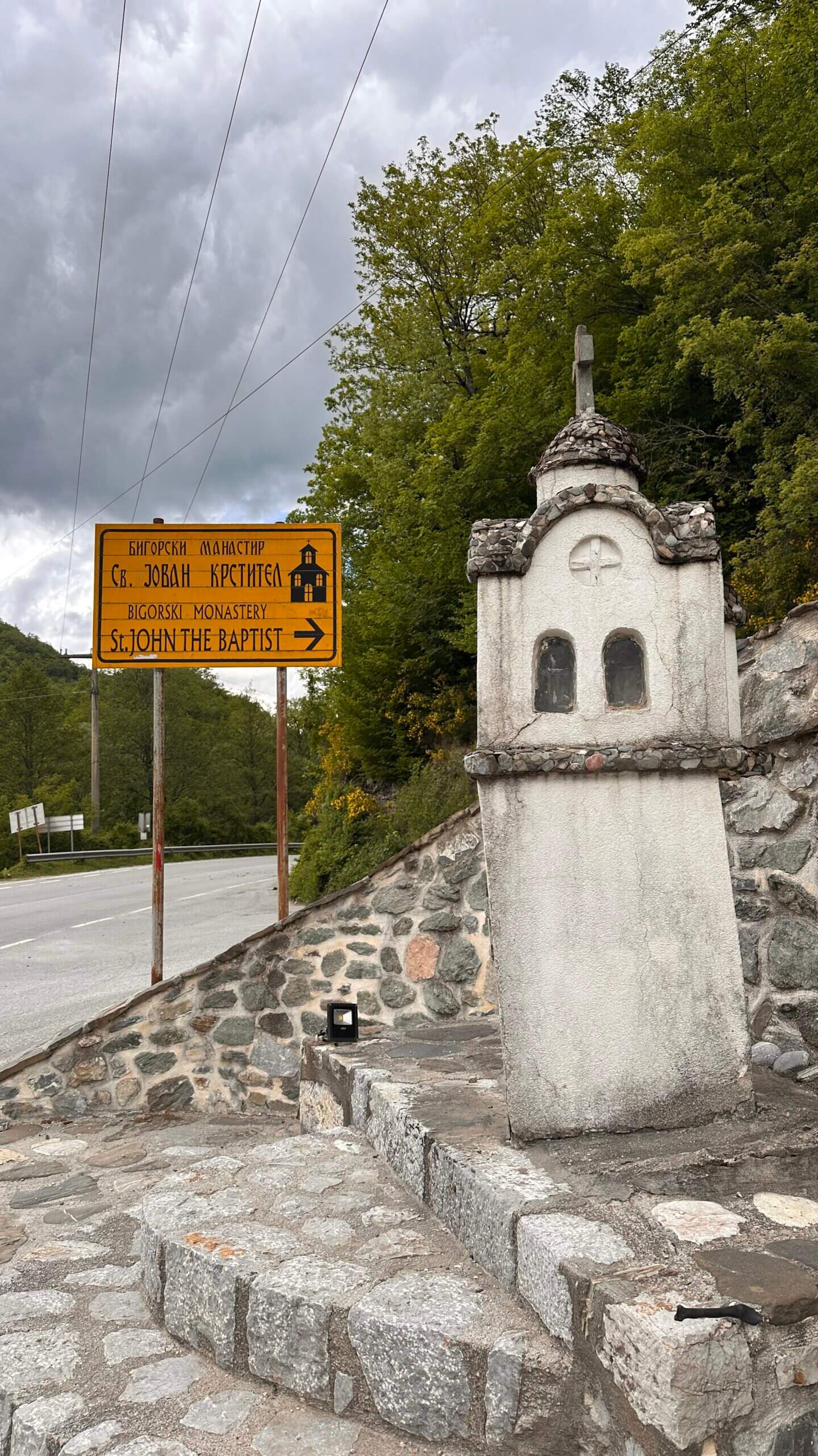 Wegschild mit Pfeil nach rechts zur St. John the Baptist Kirche vor einer Steintreppe und einer Miniaturkirche aus Stein im Mavrovo Nationalpark