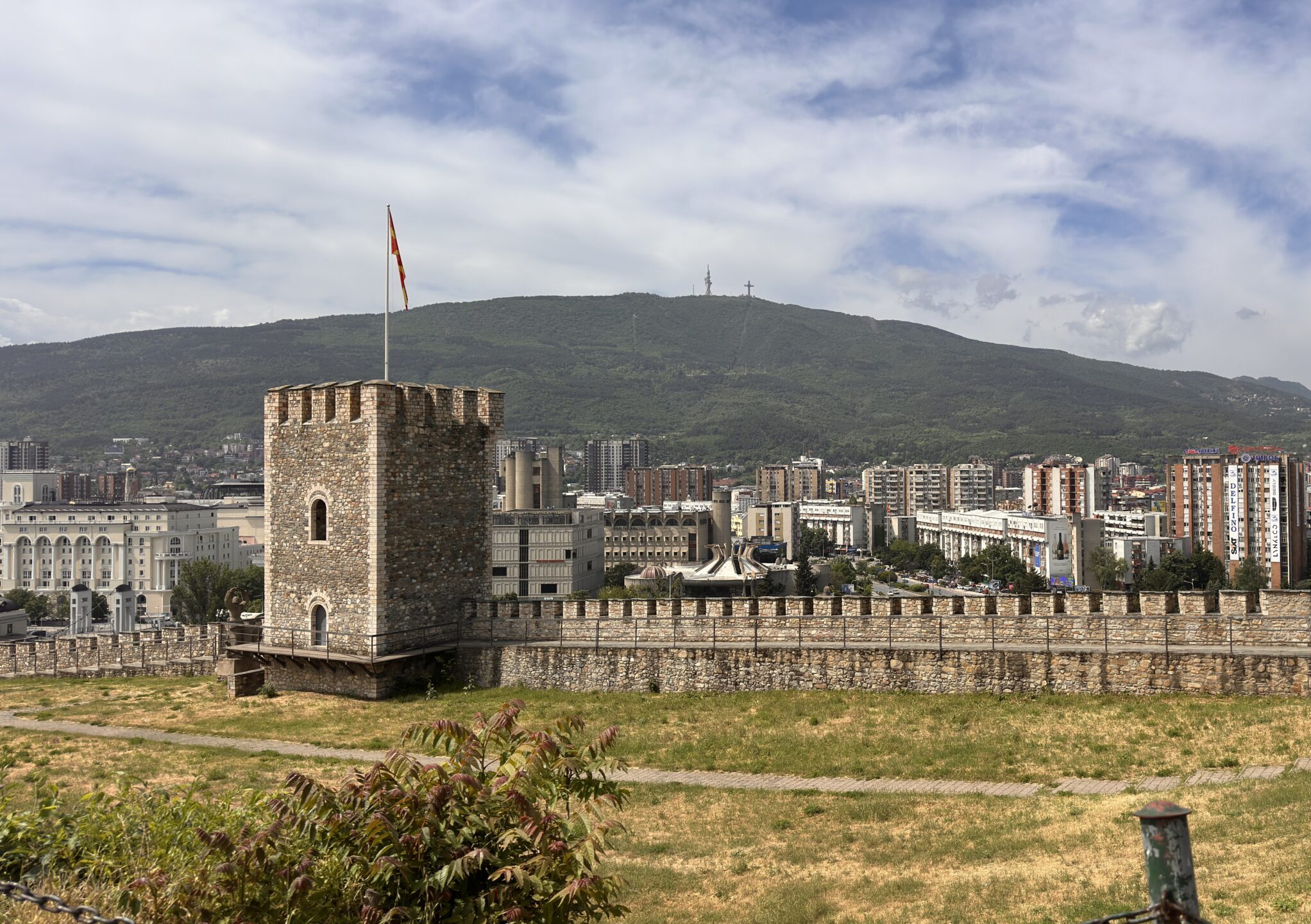 Blick auf Stadt von der Skopje Festung aus mit Wachturm und Flagge im Vordergrund hinter grüner Wiese und Berg im Hintergrund