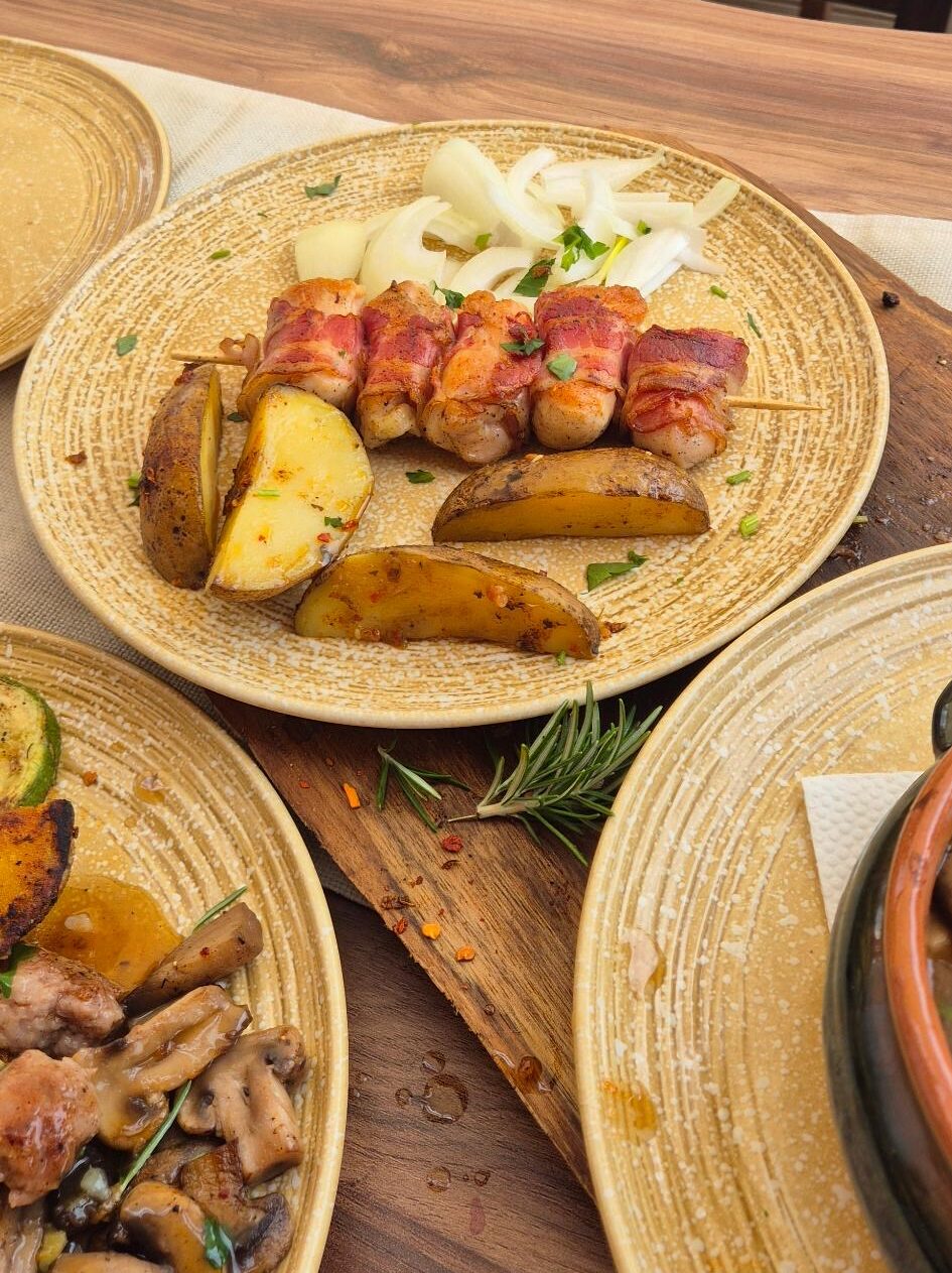 Mit Bacon umgewickelte Hähnchenspieße mit Kartoffeln und Zwiebeln auf einem Teller angerichtet im Restaurant Dedo Cane in Skopje