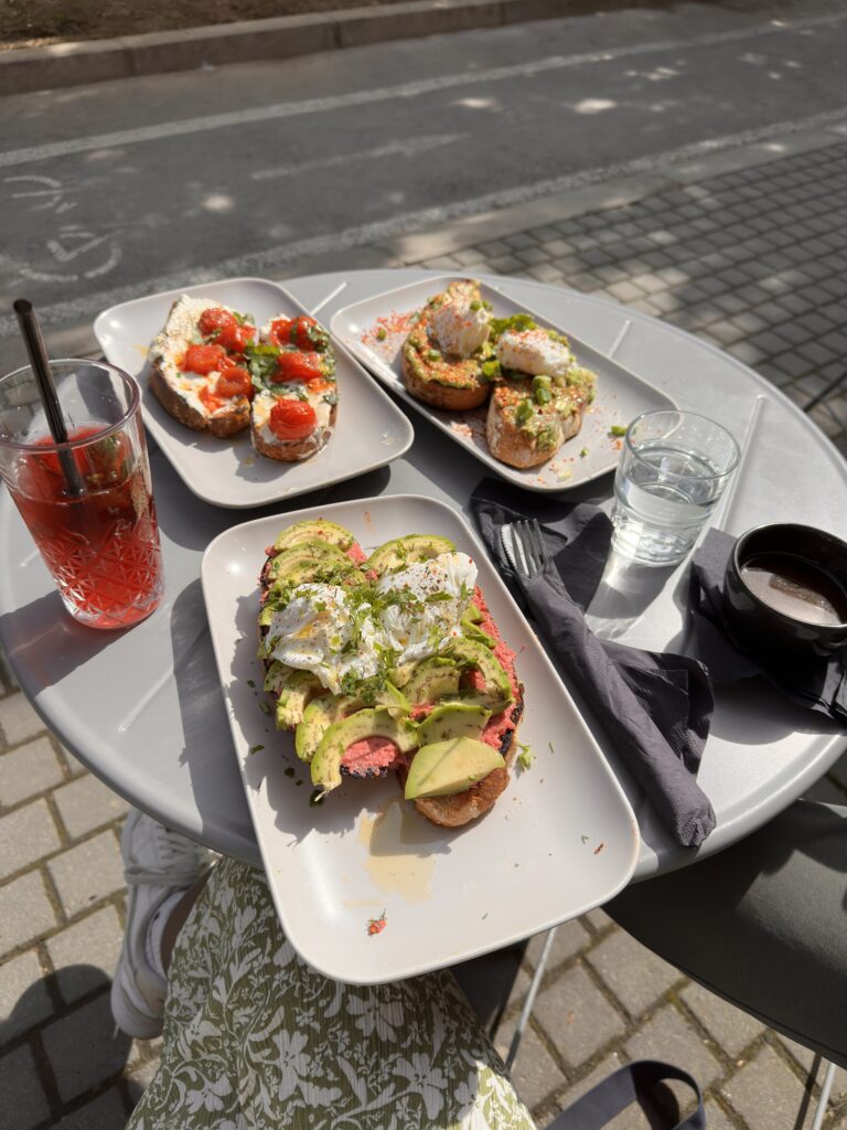 Drei Teller mit Frühstücks-Toast mit Tomaten-Ricotta-Creme und Avocado, dazu ein Café und ein Cranberry-Eistee