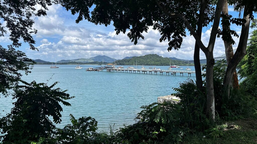 Anlegesteg am Panamakanal mit Segelbooten und Yachten vor grünen Hügeln, gerahmt von tropischen Bäumen