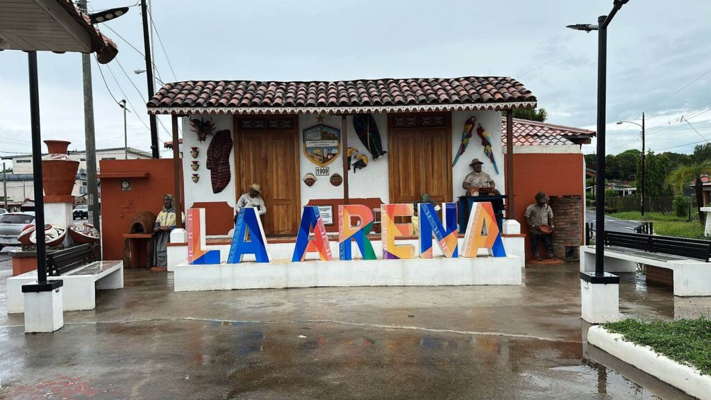Bunter Schriftzug "La Arena" vor traditionellem Haus mit Töpferfiguren in La Arena Panama